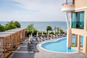 a resort with a swimming pool and chairs and the ocean at Grand Hotel Sveti Vlas - Fitness & SPA Hotel in Sveti Vlas