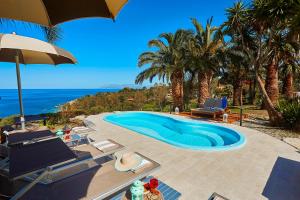 a swimming pool with chairs and an umbrella at Villa Gabbiano - Scopello-Villas in Scopello