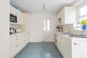 a white kitchen with white cabinets and a sink at Captains Cottage in Deal