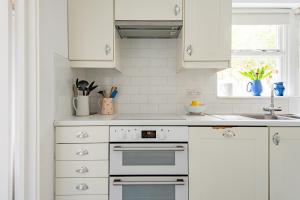 a white kitchen with white cabinets and a sink at Captains Cottage in Deal