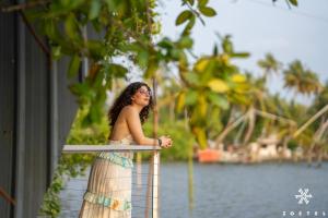 a woman in a dress leaning on a railing near the water at Zostel Kochi, Kumbalangi in Cochin