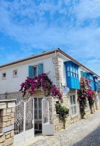 a white building with blue windows and purple flowers at Mavi Konak Alaçatı in Alaçatı