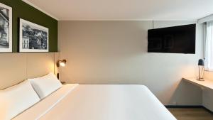 a bedroom with a white bed and a flat screen tv at Campanile NATURE - Meaux in Meaux