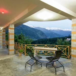 a balcony with two chairs and a table and mountains at Monal House in Manāli