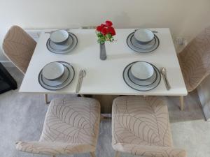a white table with plates and a vase with red flowers at 2 Bedrooms Flat in Surrey, 30 min to London in Woking