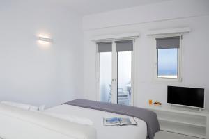 a white bedroom with a bed and a flat screen tv at Blue Vice Megalochori in Megalochori