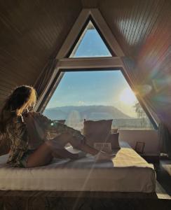 a woman sitting on a bed looking out a window at Kapa Chalet Bran in Sohodol