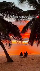 two people sitting on chairs under a palm tree on the beach at Sunset Combate in Cabo Rojo