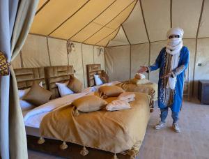 a man standing in a tent with four beds at Grand Dunes Luxury Camp in Merzouga