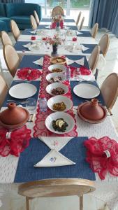 a long table with white plates and red flowers on it at Chambres d'hôtes - Écohâme - Guitar Palace in Ouazzane