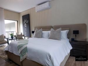 a bedroom with a large white bed and a living room at Pitzer Suites in Midrand
