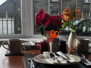 a table with plates and cups and a vase with flowers at Lomond Guest House in Leven +22 photos