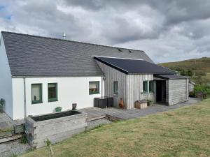 a white house with a deck in front of it at Modern, eco friendly house in Kildonan on Skye in Flashader
