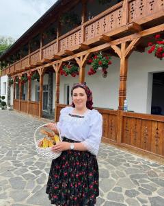 a woman holding a basket of food in front of a building at Conacul Birtoc Refugiu Tradițional în Maramureș in Văleni