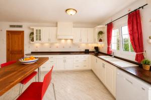 a kitchen with white cabinets and a wooden table and red chairs at Villa Savanna Spacious villa with private pool near the beach in Cala en Blanes