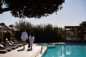 a man and woman walking by a swimming pool at Malena Hotel & Suites - Adults Only by Omilos Hotels in Amoudara Herakliou