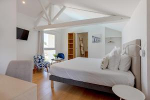 a white bedroom with a bed and a chair at Hôtel Le Square in Saint-Pierre-dʼOléron