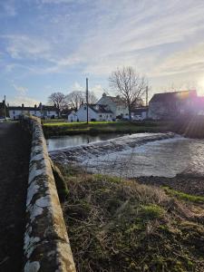 a stone wall next to a river with houses at Brook cottage in Brayton Station