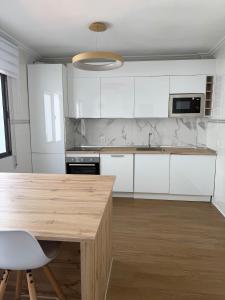 a kitchen with white cabinets and a wooden table at Entre Plazas in Cáceres