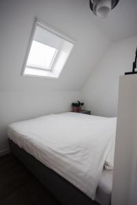 a bedroom with a white bed with a window at vredehof appartement in Sint Maartensbrug