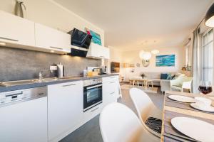 a kitchen with white cabinets and a table with chairs at Am Horizont 3 modern und stilvoll Garten Strandkorb Nähe Strand und Hafen WLAN und Parkplatz inklusiv in Zingst