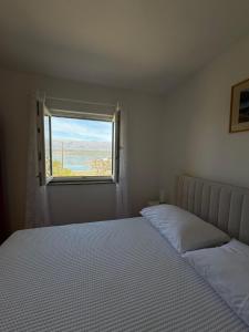 a white bedroom with a bed and a window at Apartments Mikecin in Novigrad Dalmatia