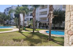 a resort with a pool and palm trees in front of a building at L'Olivier à Marina Golf Vue sur Piscine, Wi-Fi et Clim in Asilah