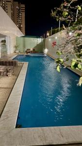 a large blue swimming pool in a city at night at Vale Hospedar Orla Apart in Petrolina