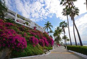 a sidewalk with pink flowers and palm trees and a building at PlayaSol las Hadas in Manzanillo