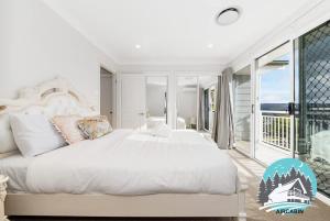 a white bedroom with a large bed and a balcony at 1B house beachside comfy stay in Collaroy