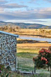 a stone building in a field with a body of water at Shepherd's Cottage at Lisdillon Estate in Little Swanport