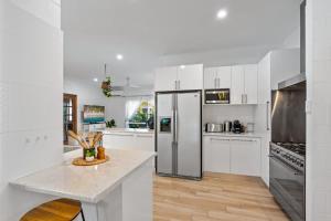 a kitchen with white cabinets and a stainless steel refrigerator at Trinity Charm - Beachside Family Getaway with Pool in Trinity Beach +12 photos