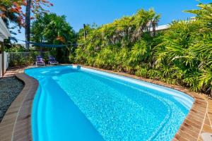 a swimming pool with blue water in a backyard with palm trees at Trinity Charm - Beachside Family Getaway with Pool in Trinity Beach