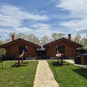 two log cabin buildings with two chairs in the grass at Căbănuțe lemn cu ciubăr in Varvata