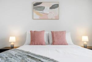 a white bed with pink pillows and two lamps at Peak Studio - Highview Haven across Shopping Centre in Cairns