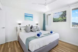 a white bedroom with a large bed with blue accents at Cairns City Escape - Elevated Modern Haven with Pool in Cairns