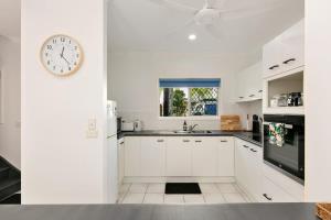 a kitchen with white cabinets and a clock on the wall at Tropical Cove at Trinity Beach with Lagoon Pool in Trinity Beach