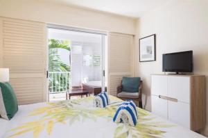 a bedroom with a bed with a television and a balcony at Couple's Coastal Haven Retreat at The Beach Club in Palm Cove