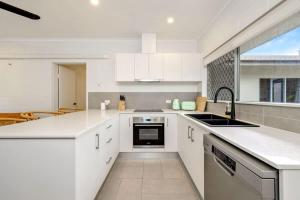 a kitchen with white cabinets and a large window at The Tropical Trinity - A Breezy Beachside Getaway in Trinity Beach
