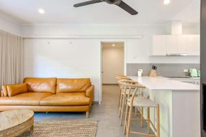 a living room with a brown leather couch and a kitchen at The Tropical Trinity - A Breezy Beachside Getaway in Trinity Beach