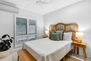 a white bedroom with a bed and a window at The Bird House - Poolside Haven a Stroll from Beach in Palm Cove