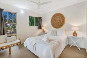 a white bedroom with a bed and a chair at Wallaby Beach House - Resort-style Comforts in Trinity Beach