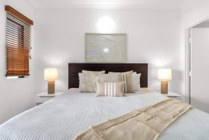 a white bedroom with a large bed with two lamps at Lagoon Lookout - Poolside Studio near Trinity Beach in Trinity Beach +14 photos