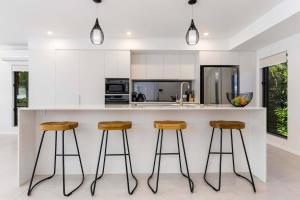 a kitchen with white cabinets and bar stools at Raphari At The Cove - A Stunning Poolside Escape in Palm Cove