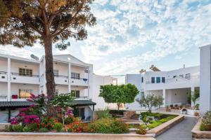 a courtyard of a white building with a tree and flowers at Elvita beach hotel in Lartos