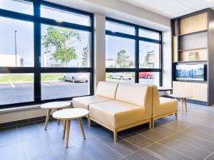 a waiting room with a couch and tables and windows at B&B HOTEL Colmar Expo in Colmar
