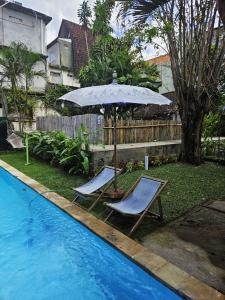 two chairs and an umbrella next to a swimming pool at Two Brothers Guesthouse in Legian