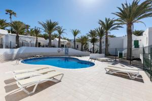 a swimming pool with two lounge chairs and palm trees at Heiwa Apartment With Pool in Costa Calma