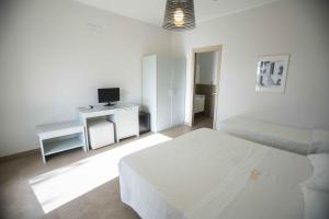 a white bedroom with a bed and a desk with a television at Hotel Sole in Lampedusa