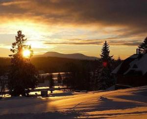 a sunset over a snowy street with the sun in the sky at Apartmány Na Kobylce in Modrava +1 photo
